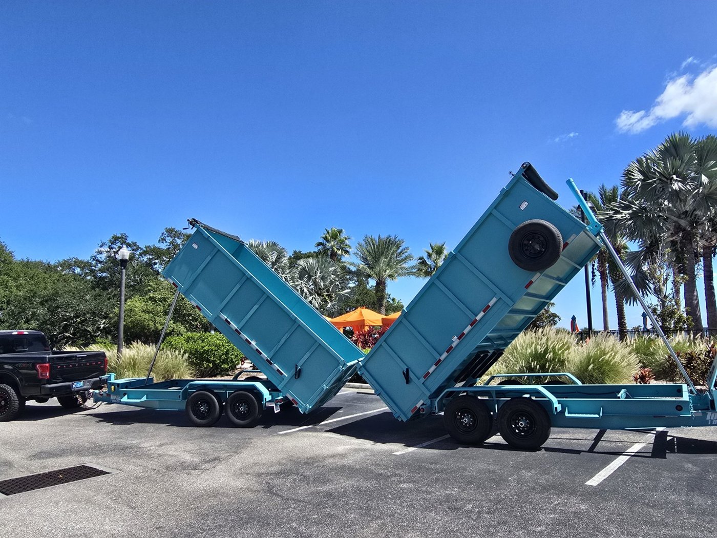 Two aqua dump trailers raised beside the hauling truck